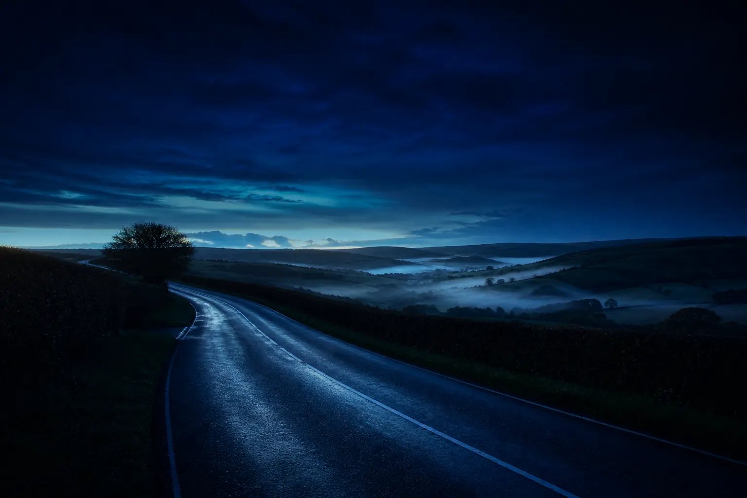 A quiet country road at dusk, with silver mist lying in the valleys of rolling English hills.